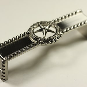May include: Silver metal drawer pull with a rope design border and a centered star design.