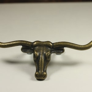 May include: A bronze-colored metal bull head with large horns. The bull head is a decorative piece with a detailed design.