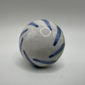 May include: White ceramic sphere with blue and green abstract designs.