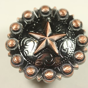 May include: A black and copper metal concho with a five-pointed star design. The concho has a decorative border with small copper circles.