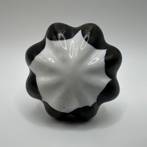 May include: A white and black ceramic knob with a scalloped edge. The knob has a starburst design.