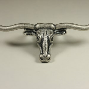May include: Silver-toned metal bull head with large horns. The bull head is a decorative piece with a detailed design.