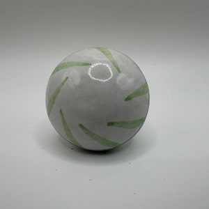 May include: White ceramic sphere with green painted lines. The sphere is smooth and glossy.