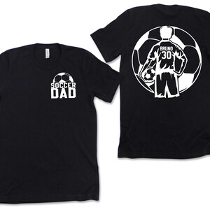 Puede incluir: Camisetas negras con dise&ntilde;os gr&aacute;ficos blancos. Una camiseta presenta "SOCCER DAD" con un bal&oacute;n de f&uacute;tbol. La otra camiseta muestra un jugador de f&uacute;tbol dentro de un bal&oacute;n de f&uacute;tbol con el nombre "Bruno" y el n&uacute;mero "30".