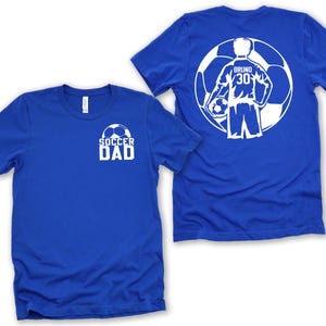 Puede incluir: Dos camisetas azul real. Una camiseta tiene el texto "SOCCER DAD" y un gr&aacute;fico de bal&oacute;n de f&uacute;tbol en la parte delantera. La otra camiseta tiene un gr&aacute;fico de jugador de f&uacute;tbol en la espalda con el nombre "BRUNO" y el n&uacute;mero "30".