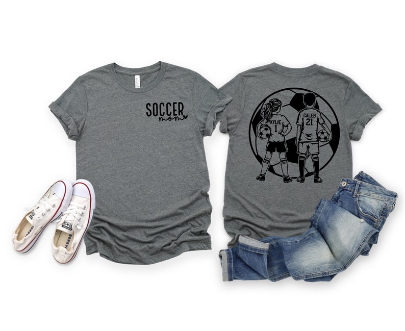 May include: Two gray t-shirts with a black soccer design on the back. The design features two soccer players, a girl and a boy, standing in front of a soccer ball. The girl's shirt says "Kylie 1" and the boy's shirt says "Caleb 21". The front of the gray t-shirt says "Soccer Mom" in black text.