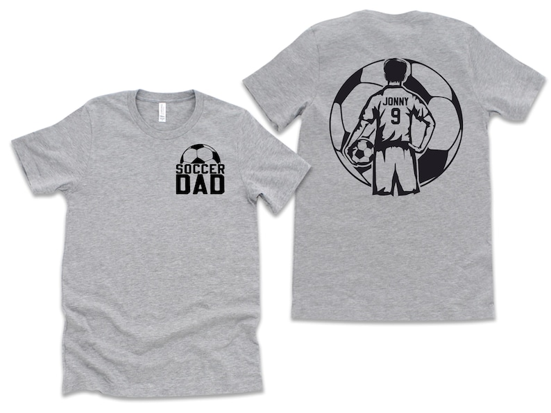 Puede incluir: Dos camisetas grises. Una camiseta tiene la inscripci&oacute;n "SOCCER DAD" en negro con un gr&aacute;fico de bal&oacute;n de f&uacute;tbol. La otra camiseta tiene un gr&aacute;fico de jugador de f&uacute;tbol en la espalda con el nombre "Jonny" y el n&uacute;mero "9".