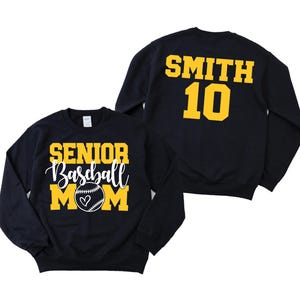 May include: Two black sweatshirts. One says "SENIOR Baseball MOM" in yellow and white with a baseball graphic. The other says "SMITH 10" in yellow. Both sweatshirts are long-sleeved.
