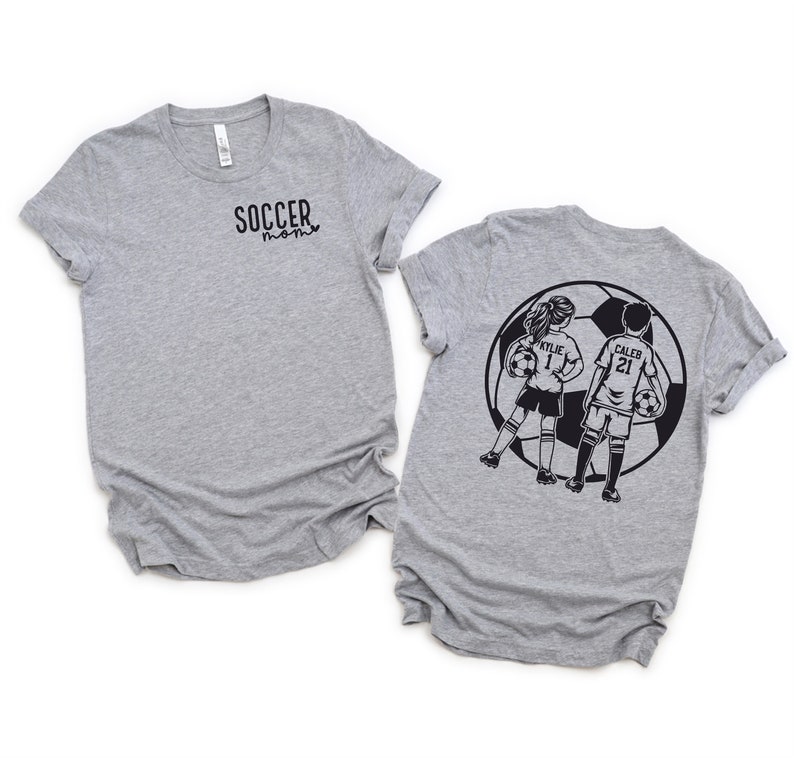 May include: Two gray t-shirts with a soccer theme. The front shirt says "Soccer Mom" and the back shirt has a graphic of two kids playing soccer with the names "Kylie 1" and "Caleb 21" on their jerseys.