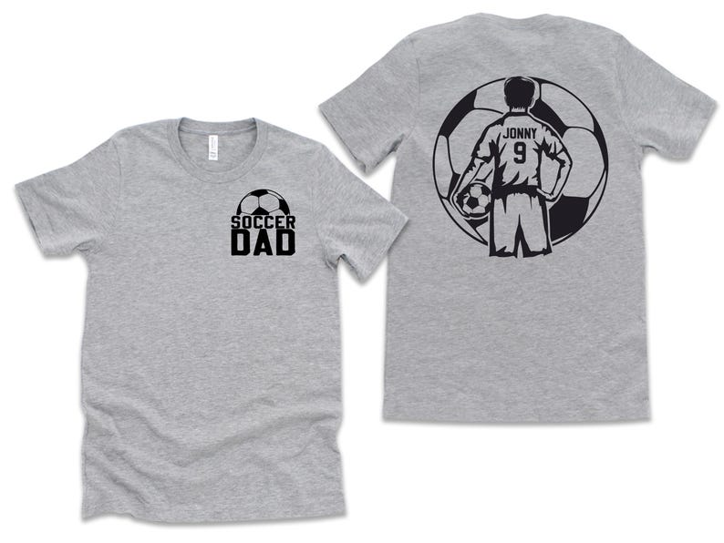 Puede incluir: Dos camisetas grises. Una camiseta tiene la inscripci&oacute;n "SOCCER DAD" en negro con un gr&aacute;fico de bal&oacute;n de f&uacute;tbol. La otra camiseta tiene un gr&aacute;fico de jugador de f&uacute;tbol en la espalda con el nombre "Jonny" y el n&uacute;mero "9".