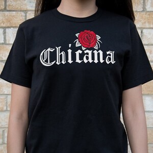 May include: Black t-shirt with a white rose and the word "Chicana" in a stylized font.