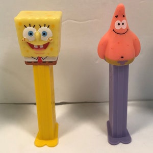 May include: Four SpongeBob SquarePants character themed candy dispensers. The dispensers are yellow, green, purple, and blue. The characters are SpongeBob, Patrick Star, Squidward Tentacles, and a yellow character wearing underwear.