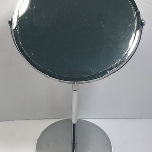 May include: A chrome-plated, freestanding vanity mirror with a round, swiveling head and a circular base.