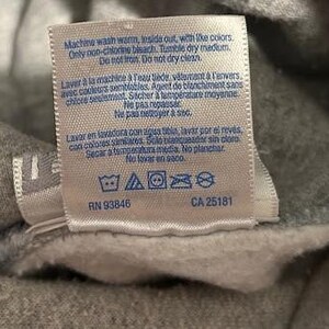 May include: A close-up of a gray fabric tag with care instructions in English and French. The tag includes washing symbols and the numbers RN 93846 and CA 25181.