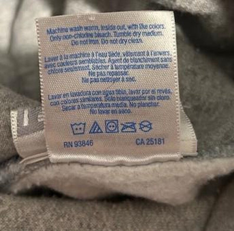 May include: A close-up of a gray fabric tag with care instructions in English and French. The tag includes washing symbols and the numbers RN 93846 and CA 25181.