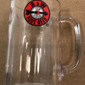 May include: A clear plastic mug with a red and white A&W Root Beer logo. The logo features an arrow pointing to the right and the words "Ice Cold" in a white circle.