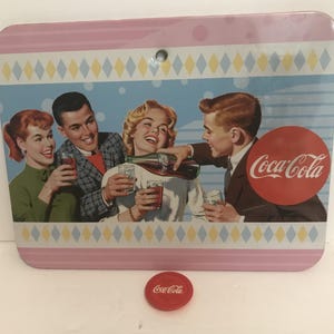 May include: A vintage-style metal sign with a pink and blue background featuring a group of four people enjoying Coca-Cola. The sign has a diamond pattern border and the Coca-Cola logo is prominently displayed in red.