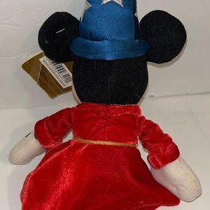 May include: A plush toy of a mouse character wearing a blue wizard hat with white stars and a red velvet robe. The toy has black ears, white gloves, and a gold belt. The toy is a collectible item.