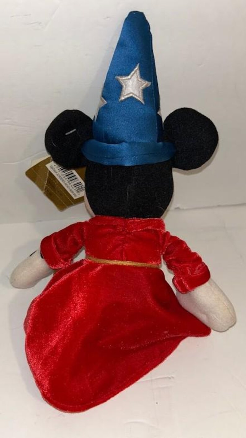 May include: A plush toy of a mouse character wearing a blue wizard hat with white stars and a red velvet robe. The toy has black ears, white gloves, and a gold belt. The toy is a collectible item.