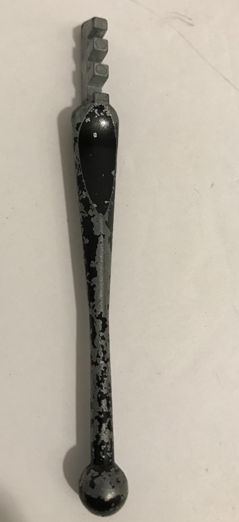 May include: A vintage glass cutter with a metal head and handle. The handle is black with silver paint chipping off, and the cutting head has multiple small wheels. The tool is designed for cutting glass.