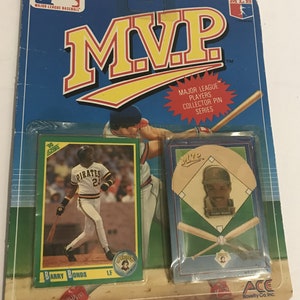 May include: A plastic package containing a baseball player collector pin featuring Barry Bonds of the Pittsburgh Pirates. The pin is gold-colored and features a portrait of Bonds wearing a Pirates uniform. The package also includes a baseball card of Bonds.