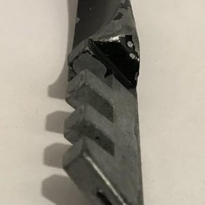 May include: Close-up of a glass cutter tool. The tool has a metal head with a series of small, grooved wheels and a black handle with chipped paint. The tool is designed for cutting glass.