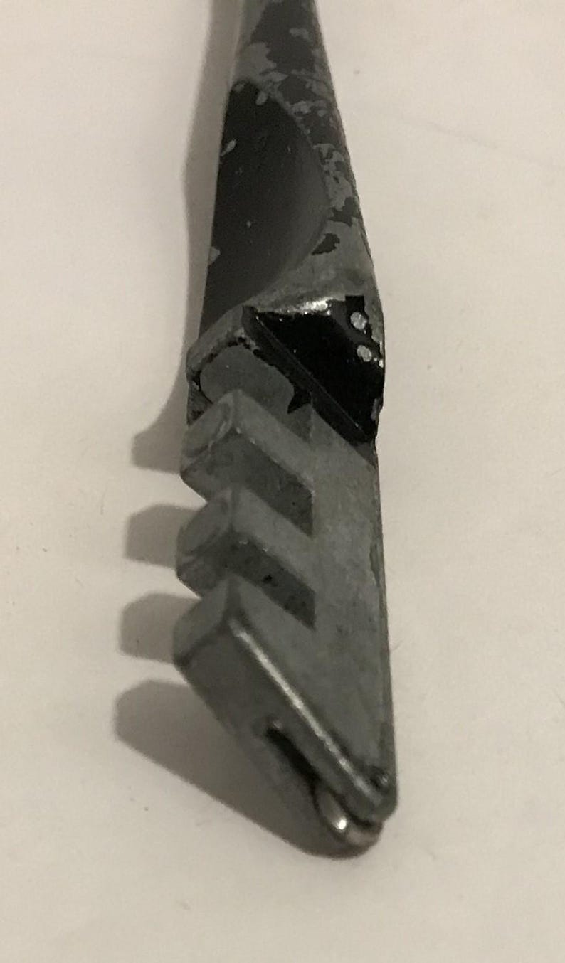 May include: Close-up of a glass cutter tool. The tool has a metal head with a series of small, grooved wheels and a black handle with chipped paint. The tool is designed for cutting glass.