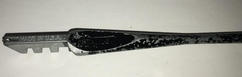 May include: A glass cutter tool with a silver metal head and a black handle. The head has a series of small teeth for scoring glass. The handle has a worn, speckled appearance. The text "MADE IN U.S.A." is visible on the head.