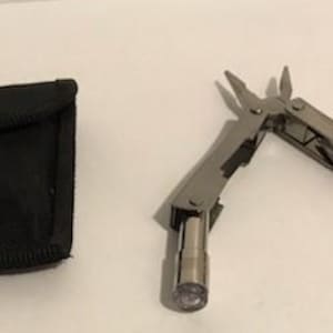 May include: A silver multi-tool with a flashlight and a black nylon carrying case.