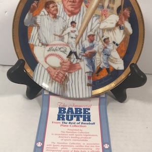 May include: A decorative porcelain plate featuring Babe Ruth in various baseball poses, with a gold rim and a blue border. The plate includes the text "Yankee Stadium" and a certificate of authenticity.