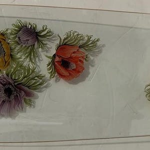 May include: A rectangular glass serving tray with a gold rim, adorned with floral illustrations. The flowers are in shades of yellow, purple, and red, with green foliage. The tray has rounded corners.