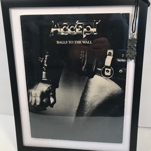 May include: A framed black and white photo of a rock band album cover. The album cover features a man in a leather jacket and jeans. The album title is "Accept Balls to the Wall".