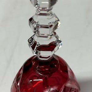 May include: A clear glass bottle stopper with a faceted, rectangular handle. The stopper has a red, rounded base with cut glass designs. The overall design is elegant and decorative, suitable for wine bottles.