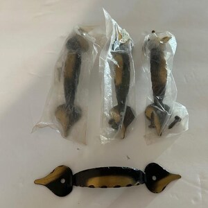 May include: A set of vintage door hardware, including three handles in plastic packaging and one larger handle. The handles are black with gold-colored accents. The hardware is designed for doors and cabinets.