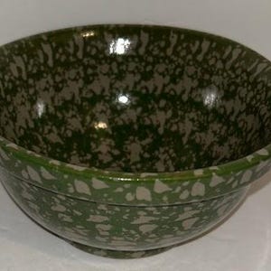 May include: A green and gray speckled ceramic bowl. The bowl has a rounded shape with a wide rim and a speckled pattern of green and gray. The bowl is likely used for serving or mixing food.