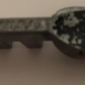 May include: Close-up of a gray metal key with the text "GS USA" embossed on the handle. The key has a worn, distressed appearance with areas of paint loss, revealing the metal beneath. The key's teeth are visible.
