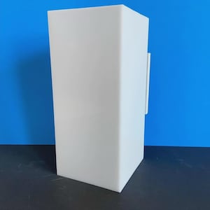 May include: A tall, white, rectangular object with a smooth surface. A thin, white, rectangular piece is attached to the side. The background is a solid blue.