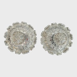 May include: A pair of silver decorative bowls with intricate floral designs. The bowls have a raised center with a floral pattern.