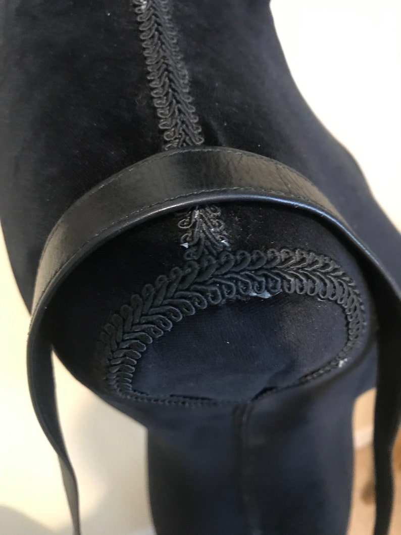 Pode incluir: Correia de couro preta com um design decorativo costurado. A correia est&aacute; presa a uma superf&iacute;cie de tecido preto.