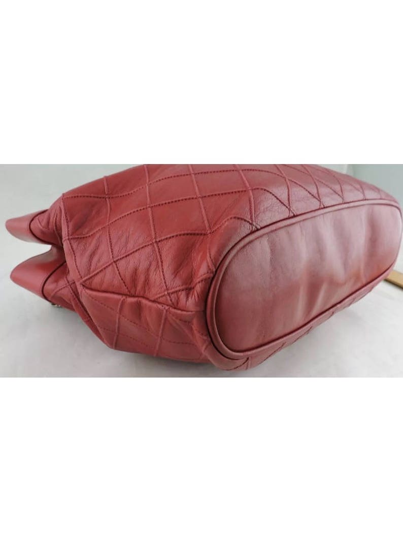 May include: A red quilted leather tote bag with a rounded bottom. The bag is made of a soft, supple leather and has a quilted design.