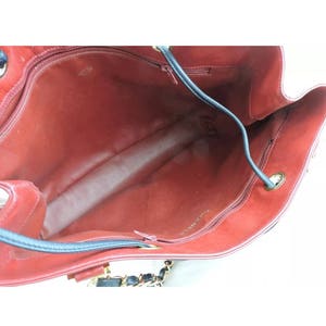 May include: The interior of a red leather handbag with a black leather trim and a gold chain strap. The bag has a zipper closure and the brand name "CHANEL" is visible on the lining.