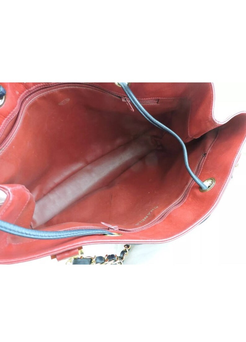 May include: The interior of a red leather handbag with a black leather trim and a gold chain strap. The bag has a zipper closure and the brand name "CHANEL" is visible on the lining.