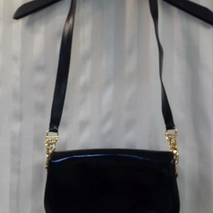 Pode incluir: Uma bolsa de ombro de couro patenteado preto com uma al&ccedil;a de corrente dourada e um fecho dourado. A bolsa tem uma forma curva e um pequeno detalhe de buraco de fechadura dourado.