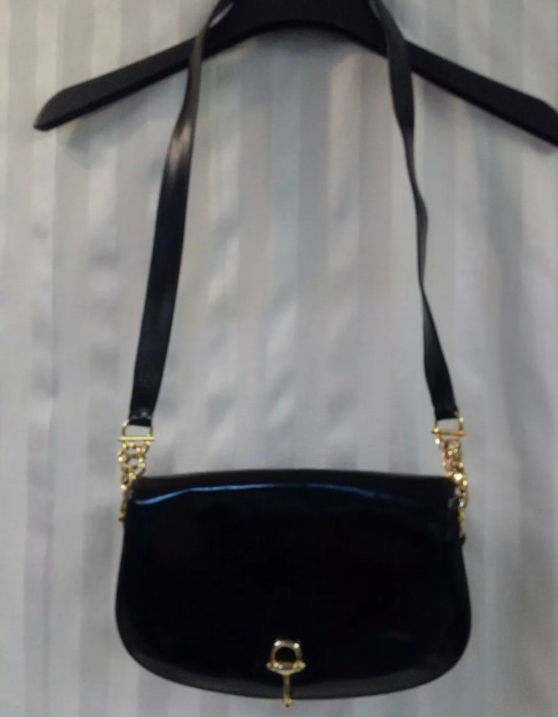 Pode incluir: Uma bolsa de ombro de couro patenteado preto com uma al&ccedil;a de corrente dourada e um fecho dourado. A bolsa tem uma forma curva e um pequeno detalhe de buraco de fechadura dourado.