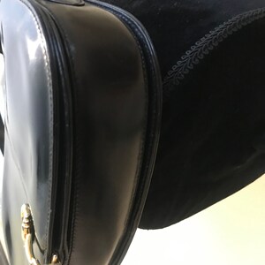 Pode incluir: Uma bolsa de m&atilde;o de couro preto com ferragens douradas. A bolsa tem fecho de aba e al&ccedil;a superior.