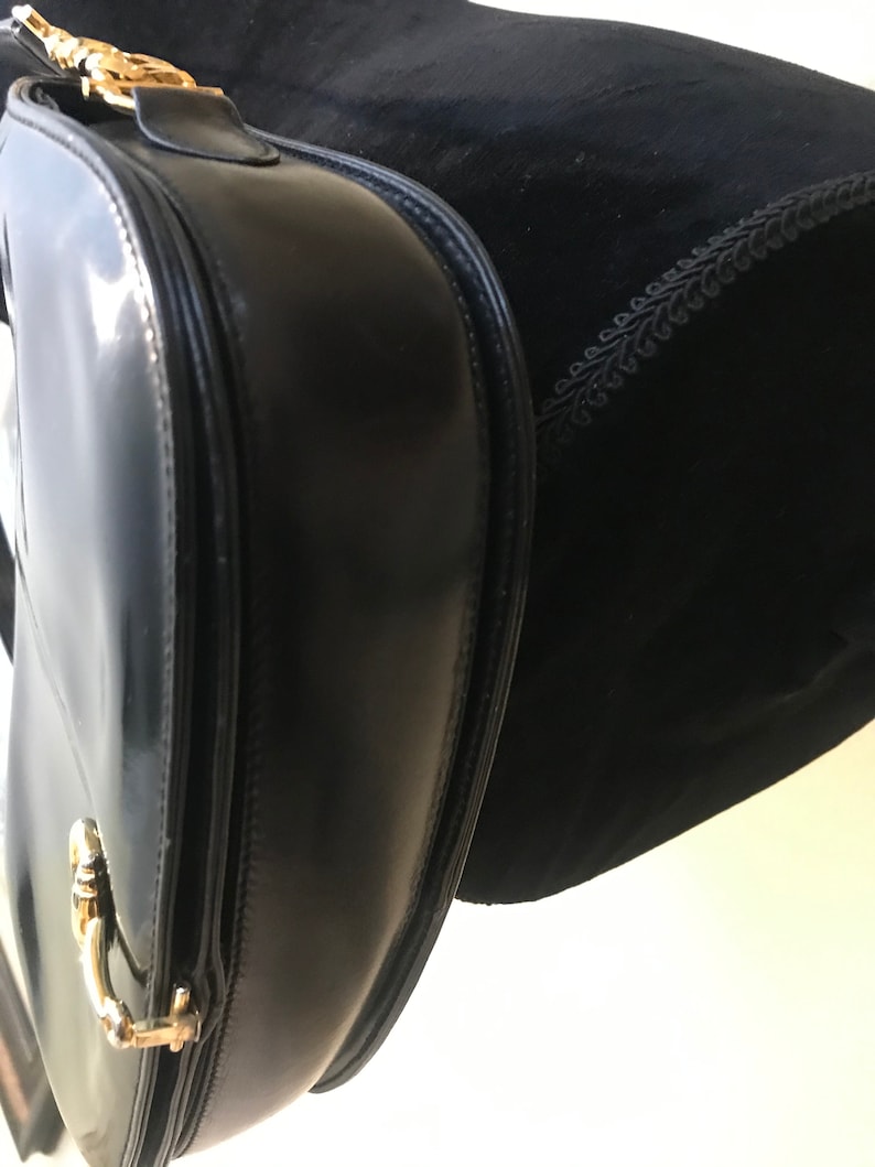 Pode incluir: Uma bolsa de m&atilde;o de couro preto com ferragens douradas. A bolsa tem fecho de aba e al&ccedil;a superior.
