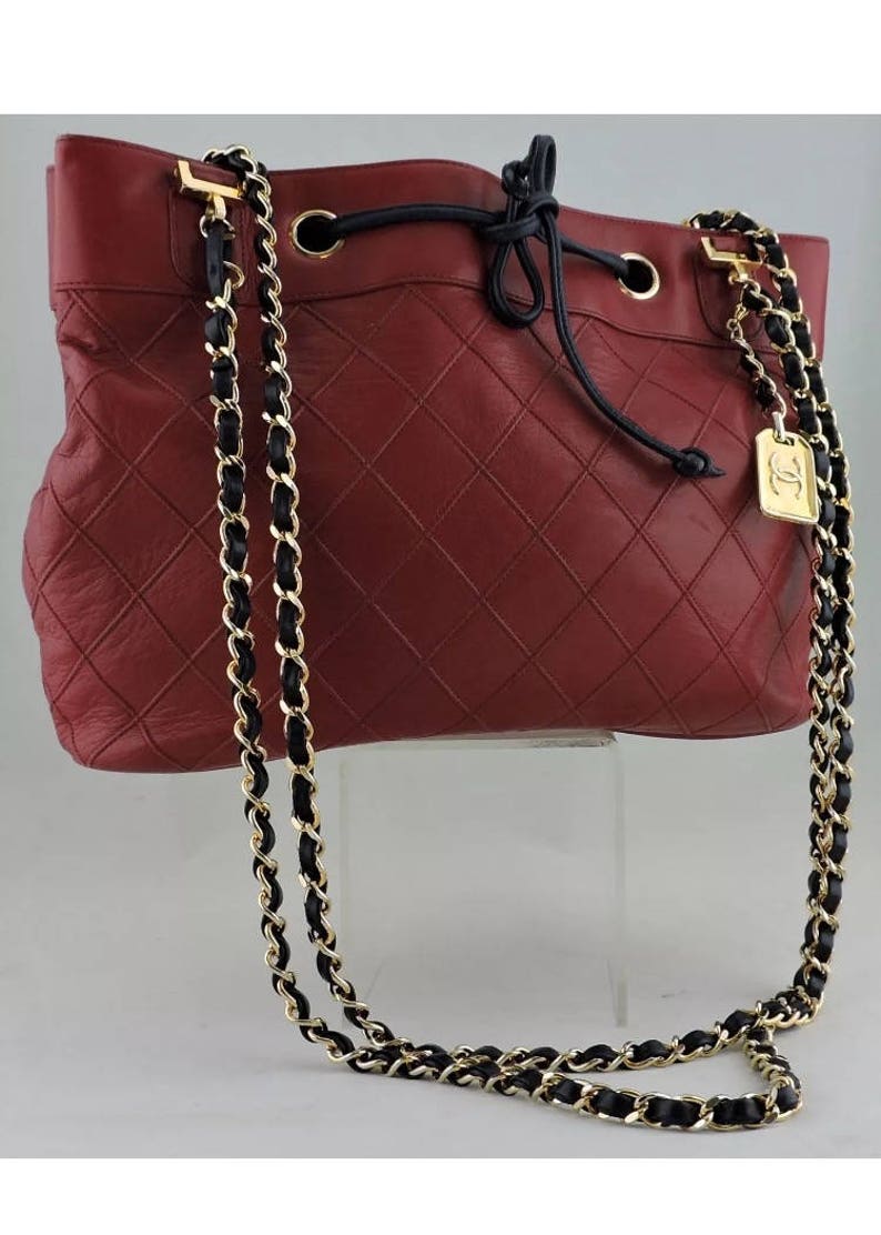 May include: A red quilted leather bucket bag with a black drawstring closure and a gold chain strap with black leather accents.