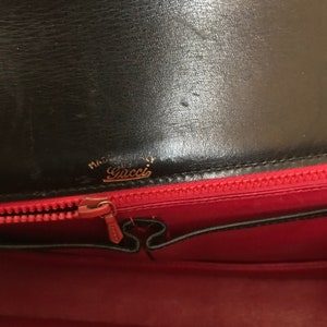 Pode incluir: O interior de uma bolsa de couro preta com forro vermelho. O z&iacute;per est&aacute; aberto e o forro &eacute; vis&iacute;vel. A bolsa tem uma etiqueta dourada que diz "Made in Italy" e "Gucci".