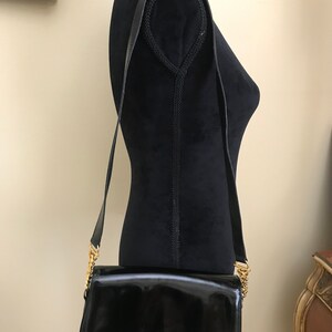Pode incluir: Uma bolsa de ombro de couro patenteado preto com uma al&ccedil;a de corrente dourada.
