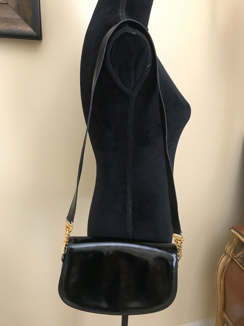 Pode incluir: Uma bolsa de ombro de couro patenteado preto com uma al&ccedil;a de corrente dourada.